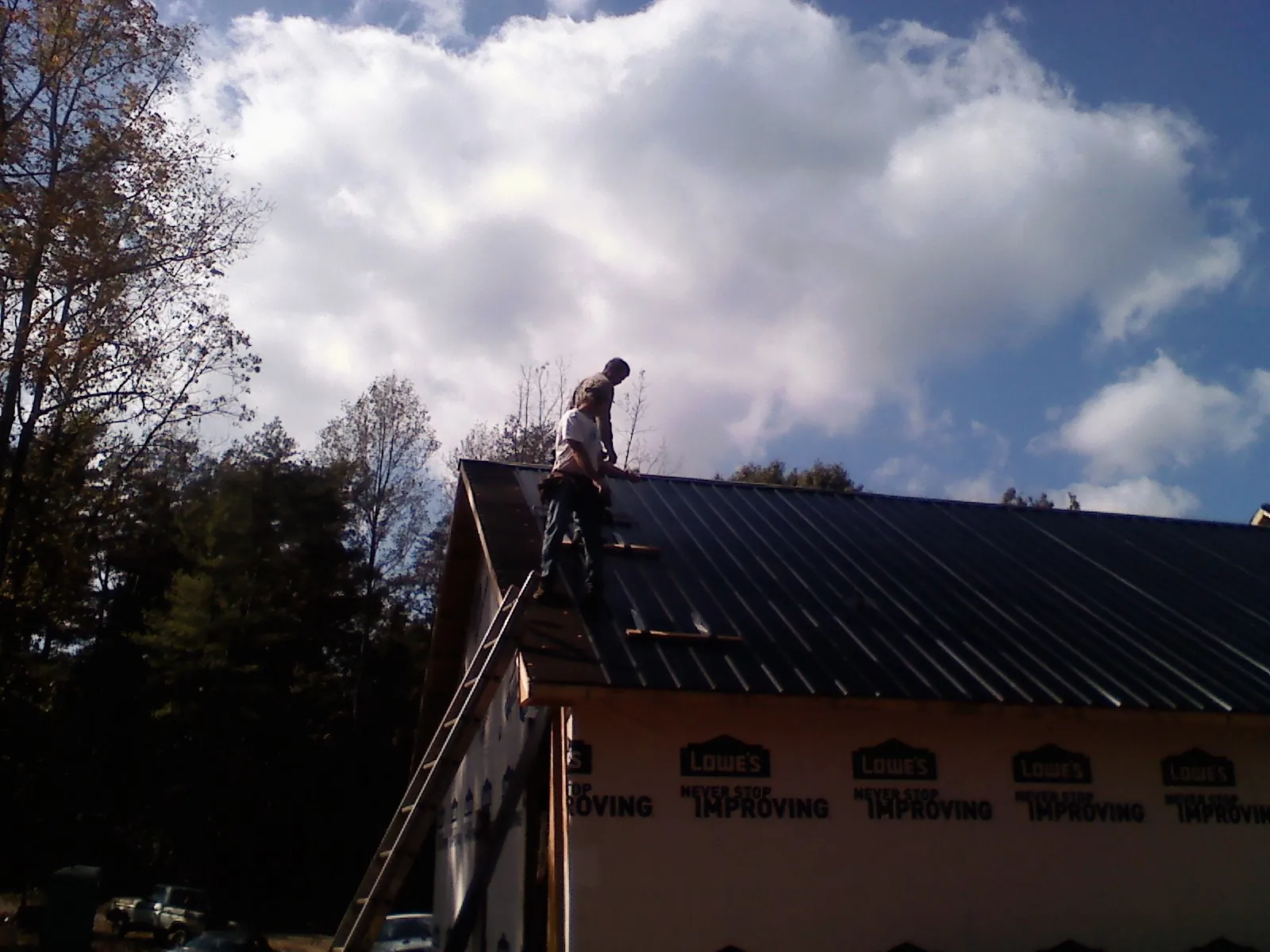 Roofer fastening dark metal panels high against a cloudy sky, from a Roof Inspection job in Garden Grove