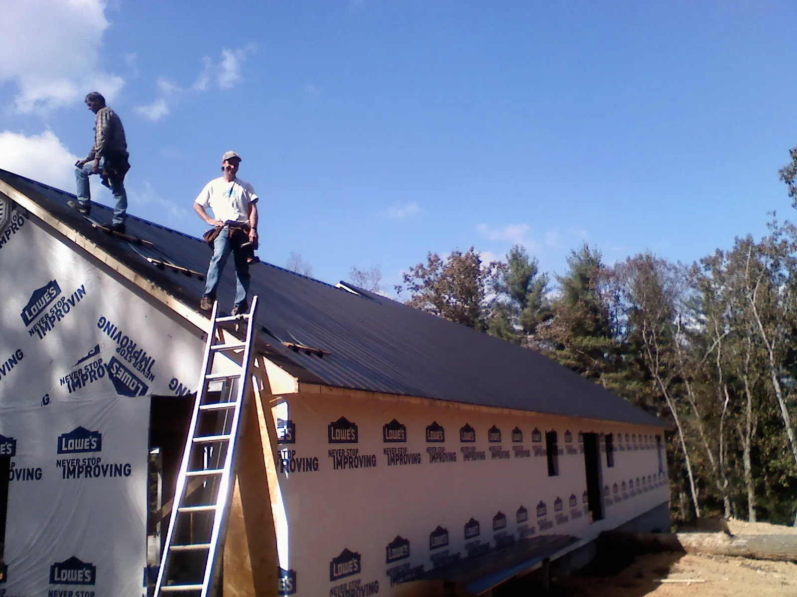 Two roofers standing on a long dark metal roof over a wrapped building in Garden Grove