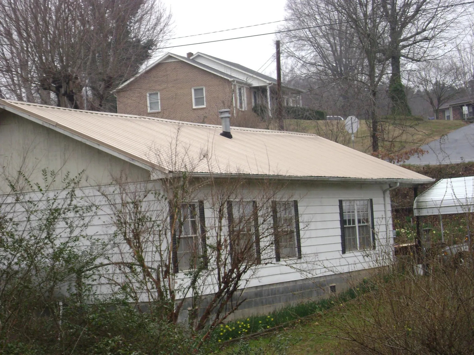 Tan metal roof on a white sided house set into a hillside — Commercial Roofing by Roofing Brothers in Garden Grove